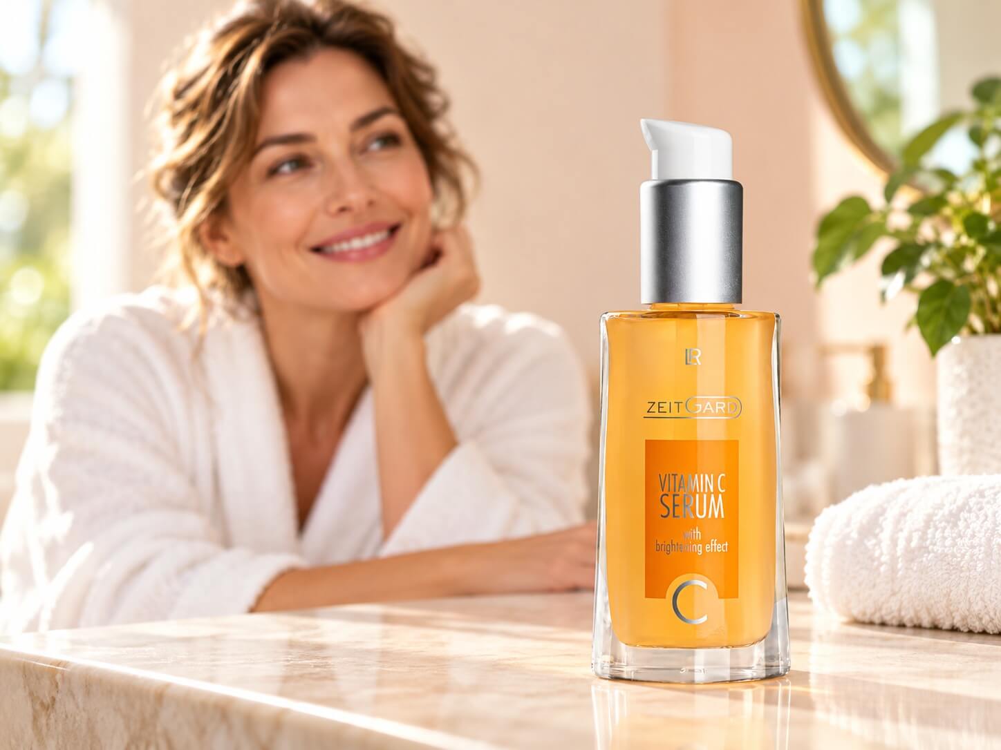 Woman in a bathrobe smiling at a bathroom counter with LR Zeitgard Vitamin C Serum